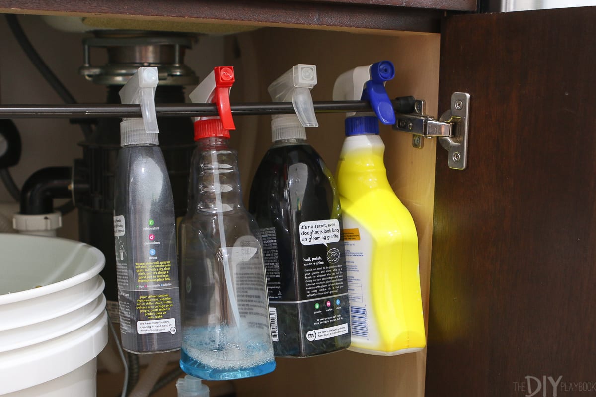 Use a tension rod as an under the sink kitchen organizer for spray bottles